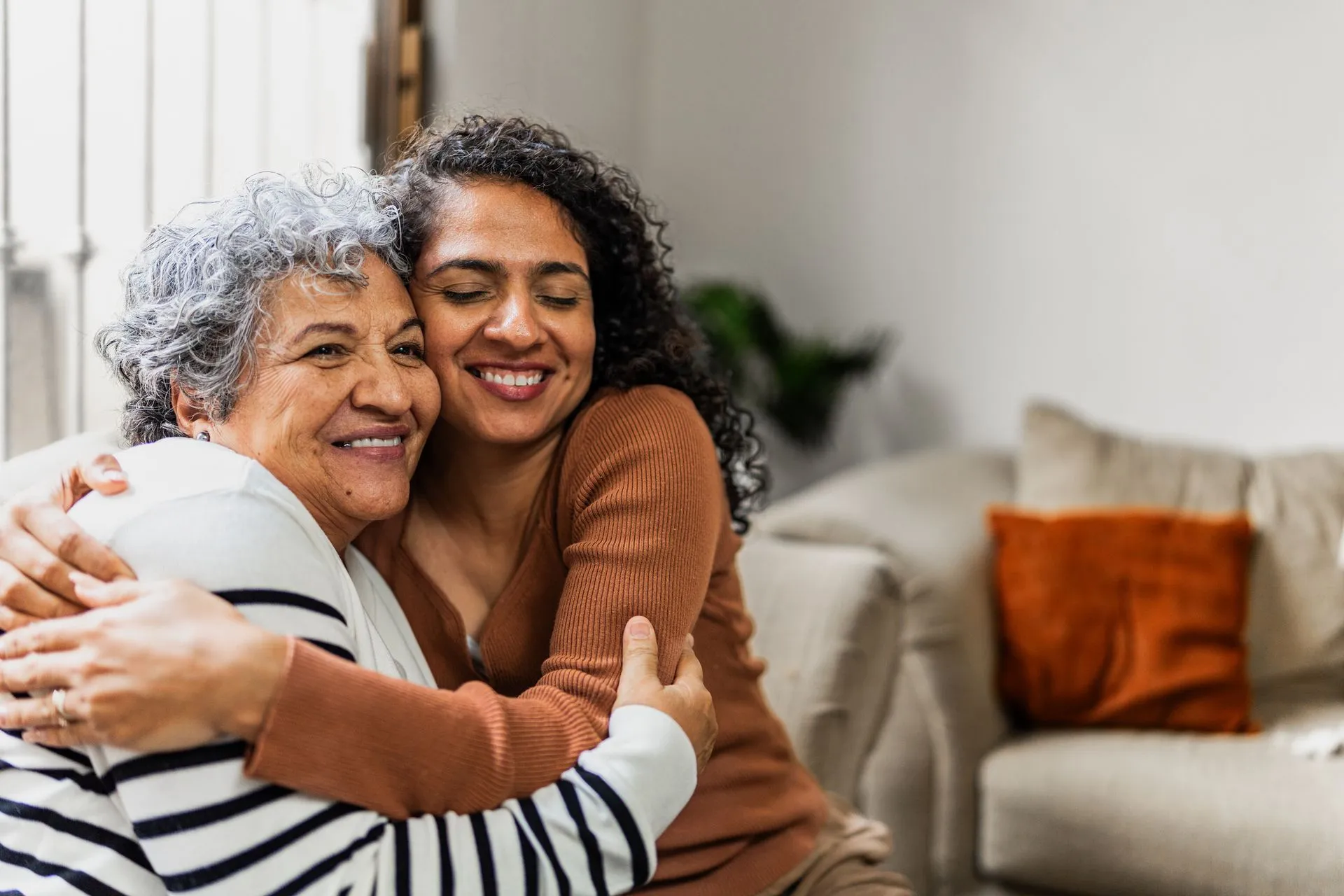 Two people smiling and hugging warmly in a bright living room.
