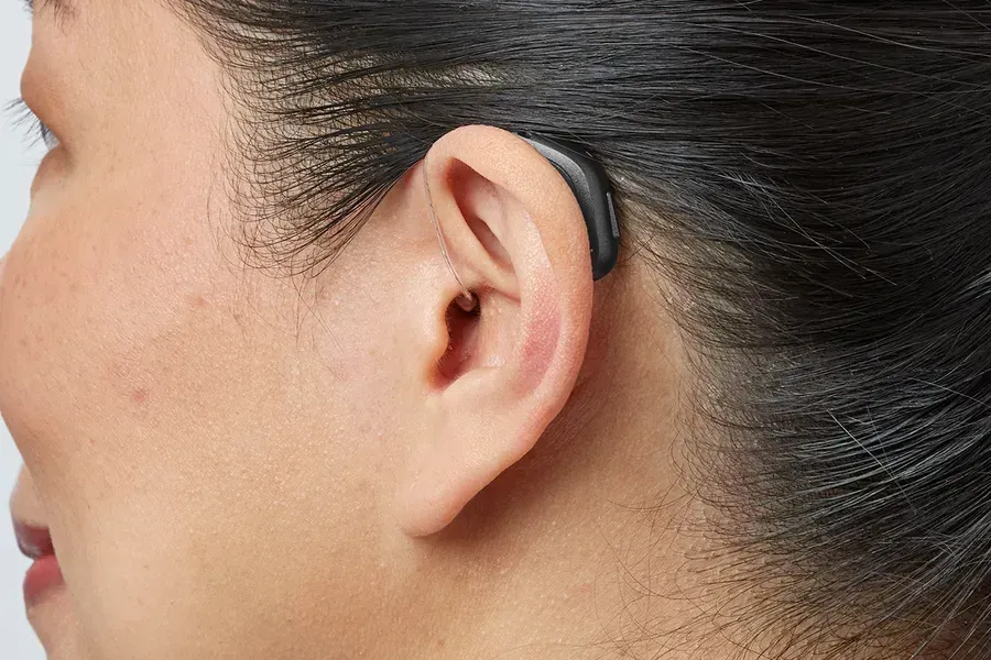 Side profile of a person wearing a discreet, dark-colored behind-the-ear hearing aid.